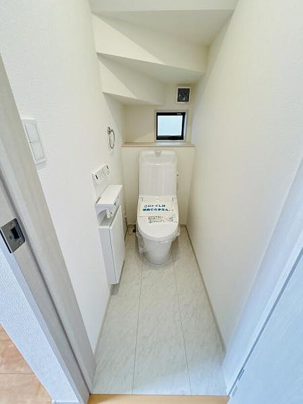 コンパクトにまとめられたトイレ空間です。小窓があり換気もしやすい設計となっています。手洗い場やペーパーホルダーも備え付けられています。床が明るい色合いで清潔感があります。