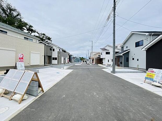新しい住宅が立ち並ぶ前面道路を含む現地写真です。道路幅も広めで車の出入りがしやすい環境です。周辺は落ち着いた雰囲気が感じられます。全体が整然としていて開放感があります。電柱や標識も整備されています。