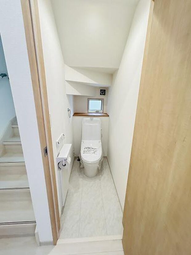 落ち着いた色合いの内装で清潔感のあるトイレです。小窓が設置されており明るさと換気が確保されています。空間を有効活用した設計になっています。戸棚スペースも便利に使えます。手洗い付きで使いやすい仕様です。
