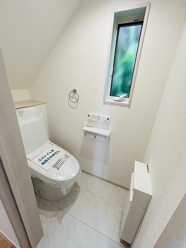 明るい窓付きのトイレは空間がすっきりとした印象です。収納スペースも確保されていて使いやすさが感じられます。壁の白さが清潔感を引き立てます。操作パネルが見やすい位置に設置されています。