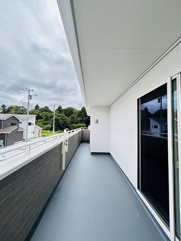 広々としたバルコニーは開放感があります。屋根付きなので天候に左右されにくい設計です。周辺の緑を感じられる眺望も魅力的です。手すりや外壁もシンプルで落ち着いたデザインです。