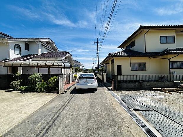 前面道路は幅があり車の出入りもしやすい環境です。周辺は住宅が立ち並び落ち着いた雰囲気が感じられます。道路沿いには整った歩道や排水溝が設けられ住環境にも配慮されています。