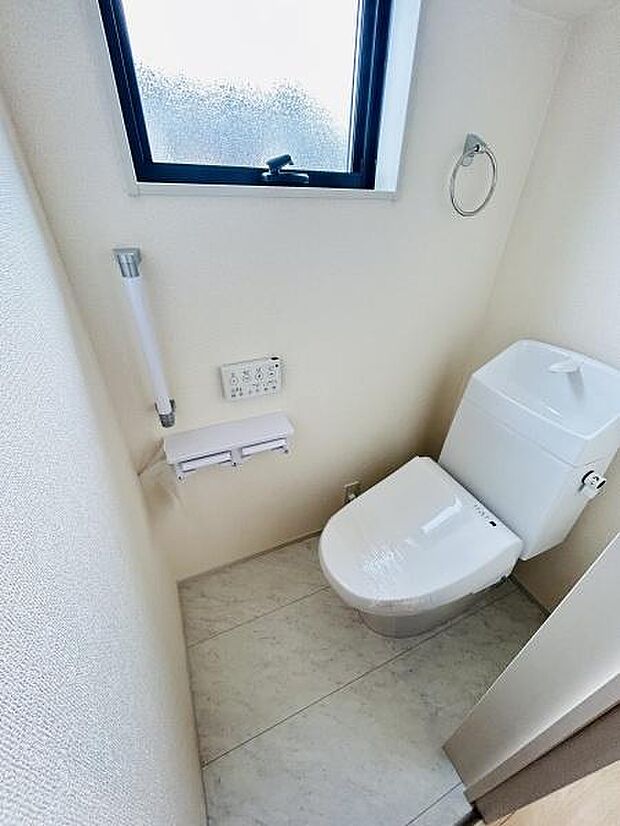窓付きの明るいトイレです。清潔感のある空間が広がっています。壁には手すりが設置されていて安心です。使いやすいペーパーホルダーや操作ボタンも揃っています。