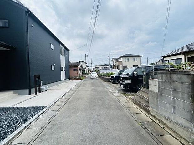 前面道路は舗装されており周辺には住宅が整然と並んでいます。道幅がしっかり確保されているため車の通行も安心です。静かな住宅街の一角で落ち着いた環境が感じられます。外観も整った現地写真です。
