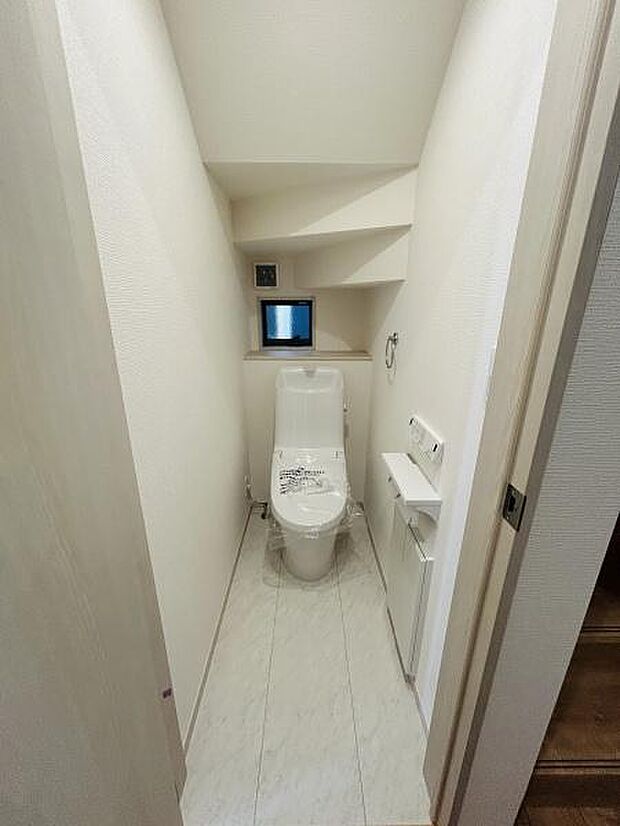 シンプルなデザインのトイレで清潔感が感じられます。小窓があり換気や採光にも配慮されています。収納棚やペーパーホルダーが設置されており使いやすさが考えられています。
