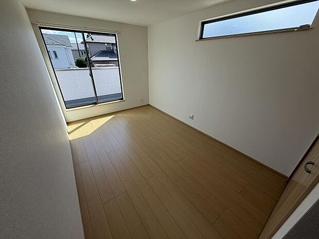 大きな窓から光が差し込む寝室です。床は木目調で落ち着いた雰囲気があります。スッキリとした壁面が広がっています。高窓もあり通風にも配慮されています。照明も天井に設置され快適に過ごせます。