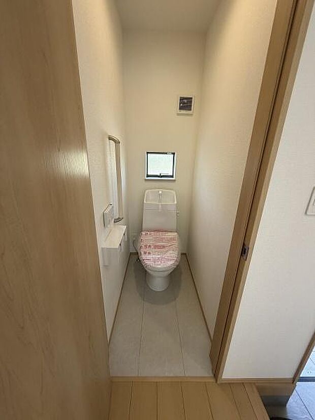 落ち着いた雰囲気のトイレ空間です。小窓から自然光が入る設計となっています。清潔感のある内装で使いやすい配置が魅力です。壁面にはペーパーホルダーが備え付けられています。