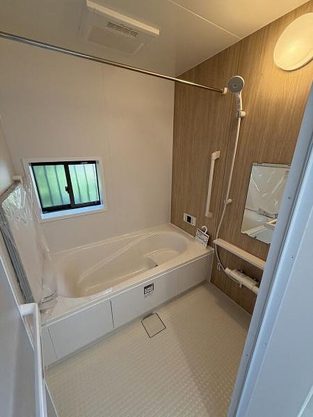 木目調のアクセントパネルが落ち着いた雰囲気を醸し出しています。浴槽はゆったりとしたサイズで手すりも設置されており安心感があります。小窓が設けられていて換気もしやすいです。