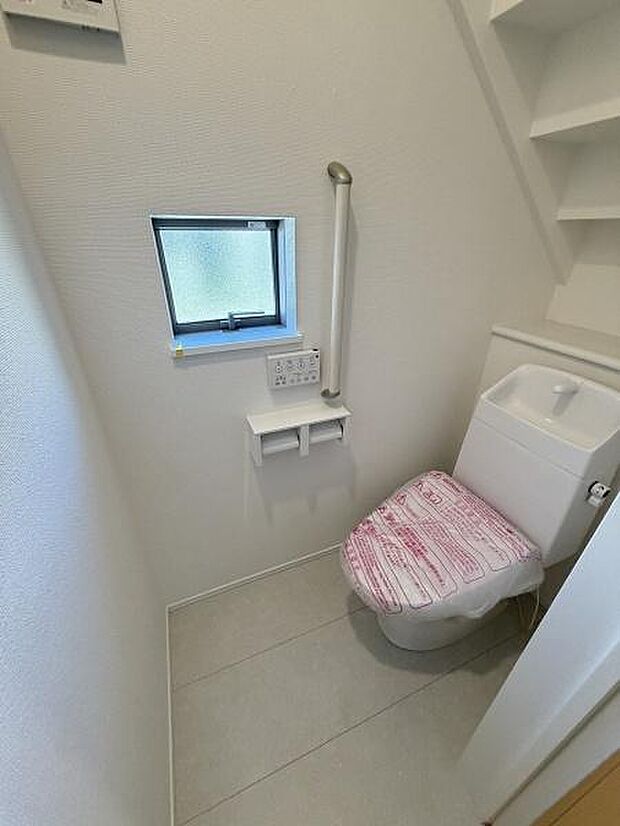 小窓付きで換気に配慮されたトイレです。手すりが設置されており安心してご利用いただけます。棚が設けられているため小物の収納も便利です。全体的に清潔感のある空間です。