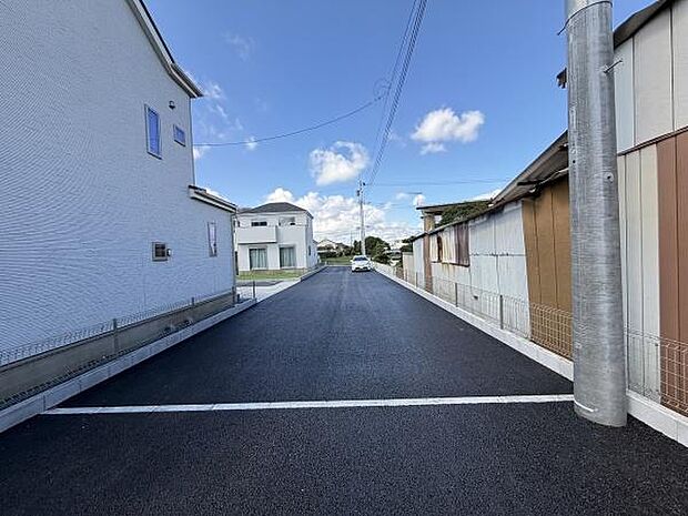 前面道路は舗装されておりすっきりとした印象です。周囲には住宅が並び見通しの良いエリアとなっています。電柱も一定間隔で設置されており整然とした街並みがうかがえます。青空が広がり明るい雰囲気です。