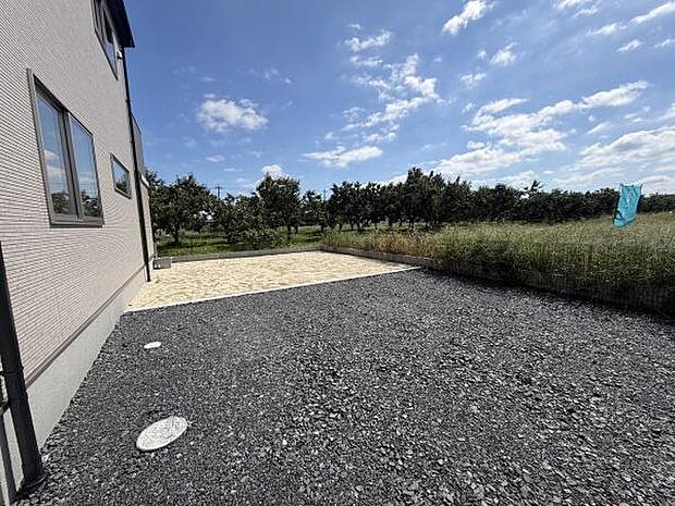 広々とした庭スペースが特徴的です。明るい空と周囲の緑が開放感を演出しています。建物横に配置されたシンプルなデザインで手入れもしやすい印象です。多目的に活用できるエリアです。