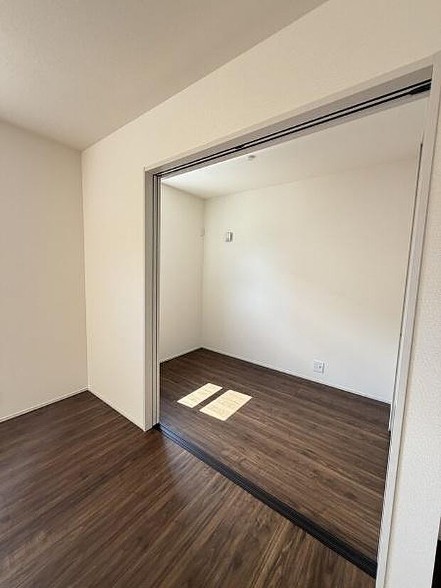 シンプルな内装が特徴の洋室です。床材の落ち着いたトーンが空間全体を引き締めています。スライドドアで仕切られており自由なレイアウトが可能です。採光もしっかり確保されています。