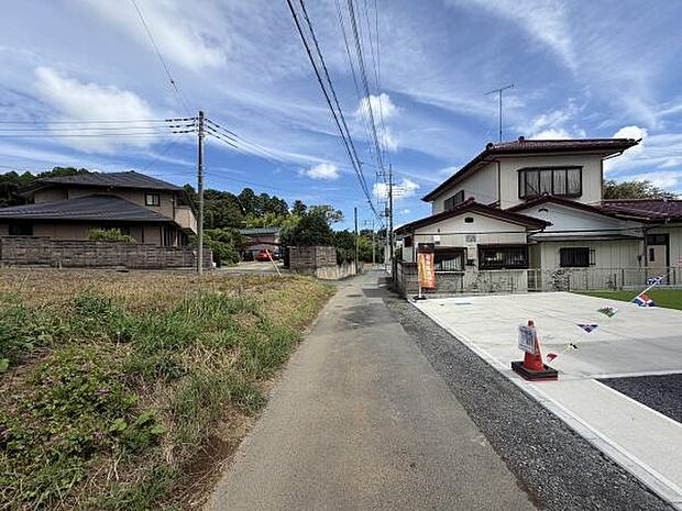 現地は落ち着いた雰囲気の前面道路沿いに位置しています。周囲には住宅や緑があり心安らぐ環境です。空が広く感じられるエリアでゆったりとした通りが印象的です。スペースの確保も容易な道路幅員となっています。