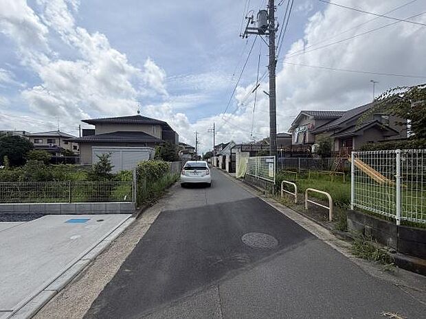 前面道路は舗装されており周囲には住宅が立ち並んでいます。電柱やフェンスも整備され落ち着いた雰囲気です。現在車両の通行も確認できますので交通アクセスを検討する際の参考になります。