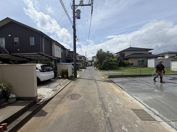 前面道路は舗装されており住宅街の落ち着いた雰囲気が感じられます。周囲には戸建住宅が並び整然とした街並みが印象的です。電柱や配線も整備されており現地の様子がよくわかる写真です。