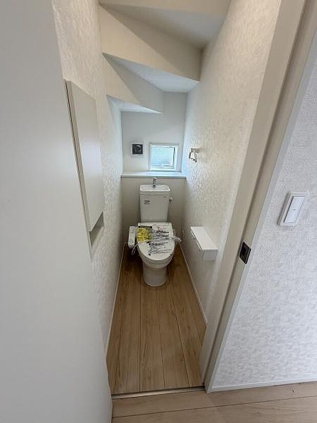 コンパクトな空間に窓があり明るさと通風が確保されています。木目調の床が空間に温かみを与えています。壁面に設置された小物置きスペースが便利です。ペーパーホルダーやタオル掛けが使いやすい配置です。
