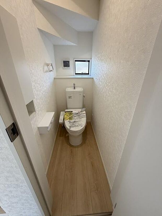 窓が設けられており換気しやすいトイレスペースです。シンプルな内装で清潔感があります。床は木目調で温かみを感じます。空間を有効活用した設計となっています。