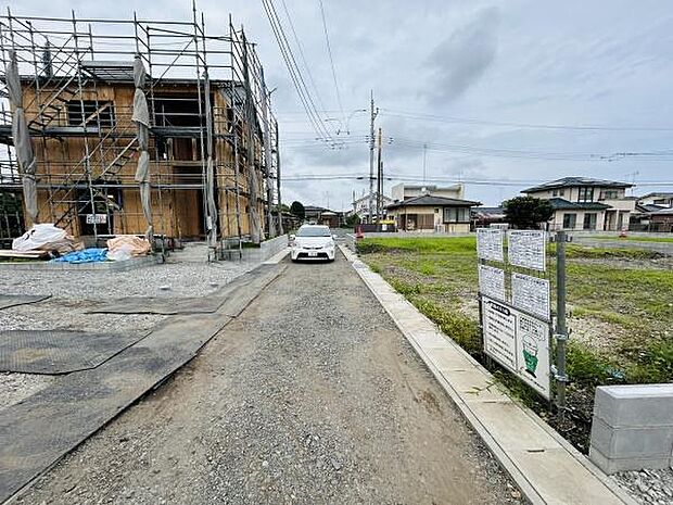現地写真では建築中の建物や車両の停車が確認できます。周辺は開放感のあるエリアで落ち着いた雰囲気が特徴です。前面道路はフラットで歩きやすく敷地の様子をしっかりご覧いただけます。