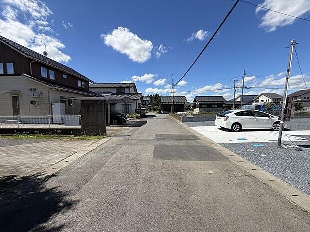 広々とした前面道路が印象的な現地写真です。車の出し入れがしやすい道幅となっています。周囲には整然とした住宅が建ち並び住環境が整っています。青空が広がり開放感のある雰囲気が感じられます。