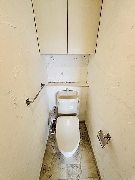 収納付きのトイレで空間を有効に活用できます。壁にはペーパーホルダーや手すりが設置されています。床のデザインが落ち着いた雰囲気を演出します。