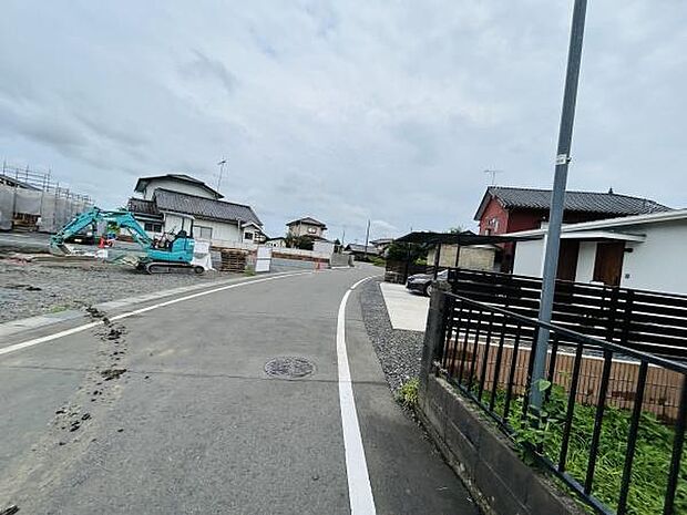 前面道路は歩道との段差が少なく車の通行もスムーズです。周辺には一戸建てが並び落ち着いた街並みが広がっています。幅のある道路で運転や移動も安心です。現地には新しい住宅建築の様子も見られます。