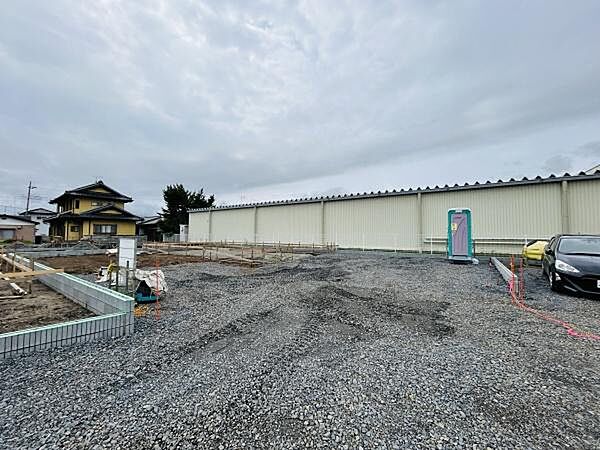 広々とした敷地が特長の土地写真です。整地済みで建築準備が進めやすい状態です。敷地の形状や周囲の環境がよく分かる写真となっています。資材置き場や仮設トイレの設置状況もご確認いただけます。