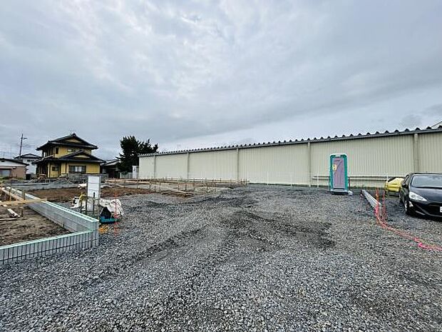 広々とした敷地が特長の土地写真です。整地済みで建築準備が進めやすい状態です。敷地の形状や周囲の環境がよく分かる写真となっています。資材置き場や仮設トイレの設置状況もご確認いただけます。