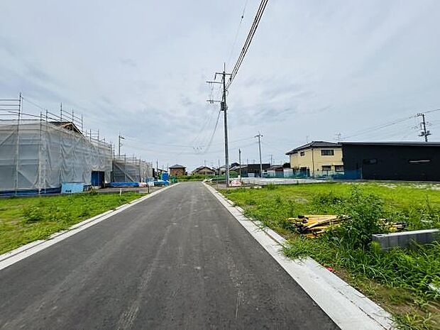 新しく整備された前面道路が印象的な現地写真です。まっすぐ伸びる道路が開放感を与えます。周囲には建築中の建物や空き区画も確認できます。住環境の変化や新たな街並みの形成を感じさせる一枚です。