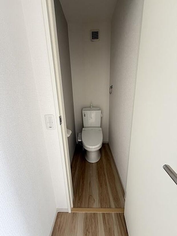 シンプルなデザインのトイレスペースです。温かみのあるフローリングが空間を引き立てます。換気設備も設置されています。無駄のないレイアウトで手入れもしやすそうです。清潔感のある壁紙が印象的です。