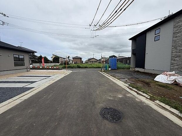 現地の前面道路は広々とした印象で車の出入りもスムーズに感じられます。周囲には新しい住宅が立ち並び街並みが整っています。舗装された道路と歩道部分が見やすく利便性が伝わります。