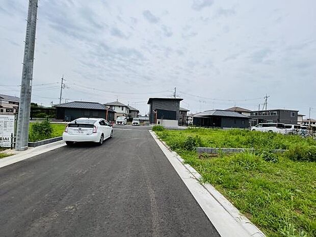 車の出入りがしやすい前面道路が特徴の現地写真です。周囲には新しい住宅が並び清潔感のある街並みです。道路幅が広く見通しの良い区画となっています。落ち着いた雰囲気のエリアで暮らしやすさを感じられます。