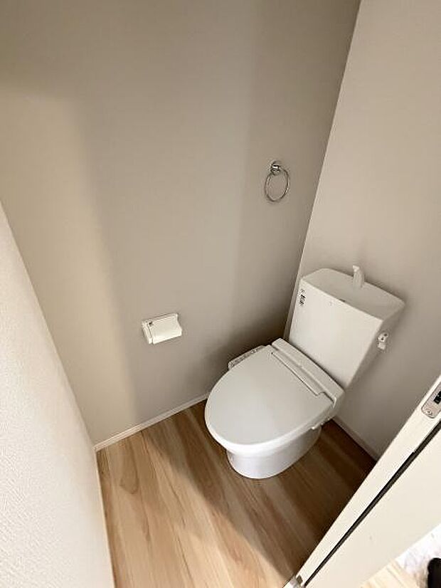 シンプルで清潔感のあるトイレです。ナチュラルなフローリングが空間全体に落ち着いた印象を与えます。壁面にタオルリングとペーパーホルダーが設置されています。手入れのしやすい設計です。