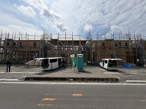 建設中の建物がしっかりとした足場で囲まれており工事の進行状況が分かる現場です。複数の車両が停車しており作業が着実に進んでいる様子がうかがえます。広々とした前面道路に面しておりアクセスにも便利です。