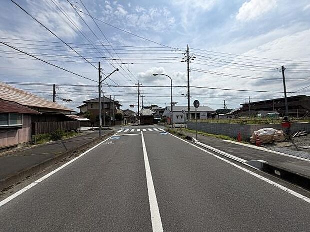 前面道路は広々とした印象で車の出入りもスムーズに行えます。周辺には整備された歩道もあり安心してご利用いただけます。住宅街の落ち着いた雰囲気が感じられる現地写真です。
