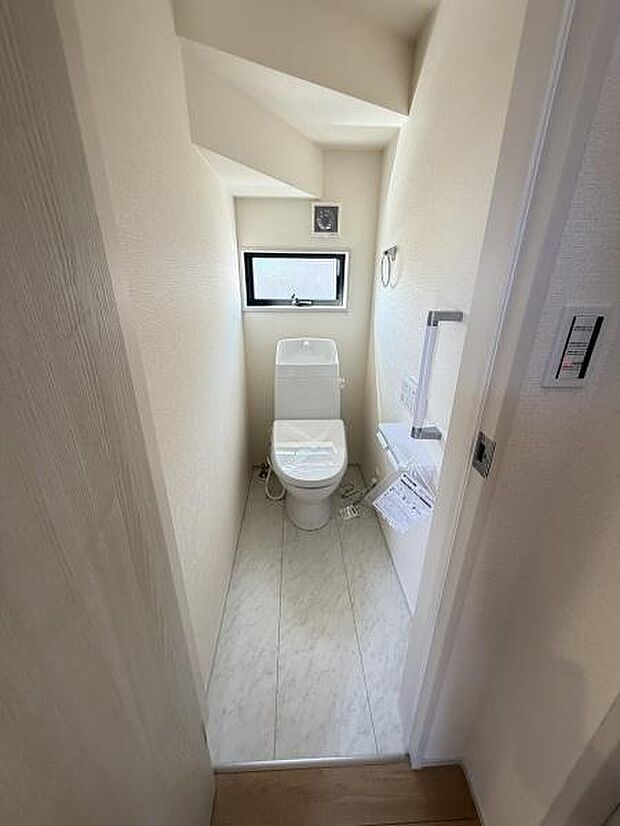 トイレには小窓が設置されており明るさと換気を確保できます。タオル掛けやペーパーホルダーも備え付けられ機能的な空間です。手洗い付きタンクで使い勝手も良好です。明るいクロスと床材で清潔感があります。