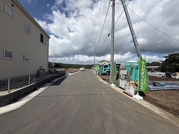 前面道路は広々としており車の出入りもスムーズに行えます。周囲には建設中の住宅が立ち並び新しい街並みが形成されています。空が広く見渡せる開放感ある現地です。道路沿いには電柱が整然と配置されています。