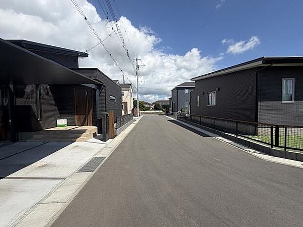 前面道路が広々としており車の出入りがしやすい現地写真です。周辺には新しい住宅が並び整った街並みが感じられます。道路は舗装がしっかりしていて安心してご利用いただけます。日当たりも良好な印象です。