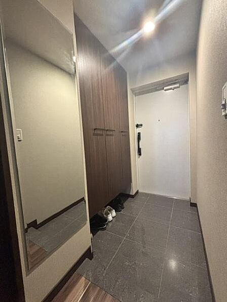玄関には大きな収納スペースが備わっています。落ち着いた色合いのタイル床で清潔感があります。全身鏡が設置されており外出前の身だしなみチェックに便利です。照明も明るくスッキリとした印象です。