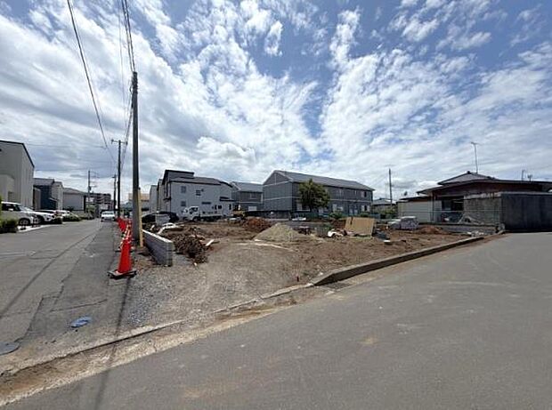 空が広く感じられる前面道路を含む現地写真です。道幅がゆったりとしており車の出入りもスムーズに行えます。周囲は住宅が建ち並び落ち着いた雰囲気のエリアです。整地された敷地の様子もはっきり確認できます。