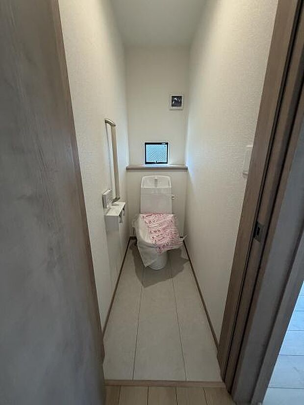 換気用の小窓が設けられており明るい空間となっています。シンプルな内装で清潔感があります。トイレットペーパーホルダーや手すりも設置されています。扉を開けたままでも広がりを感じられるつくりです。