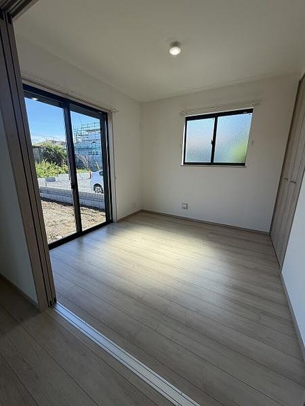 大きな窓から自然光がしっかり入る洋室です。シンプルな内装で使いやすい空間となっています。清潔感のあるフローリングが特徴的です。スライドドアで開放感もあります。収納スペースも確保されています。