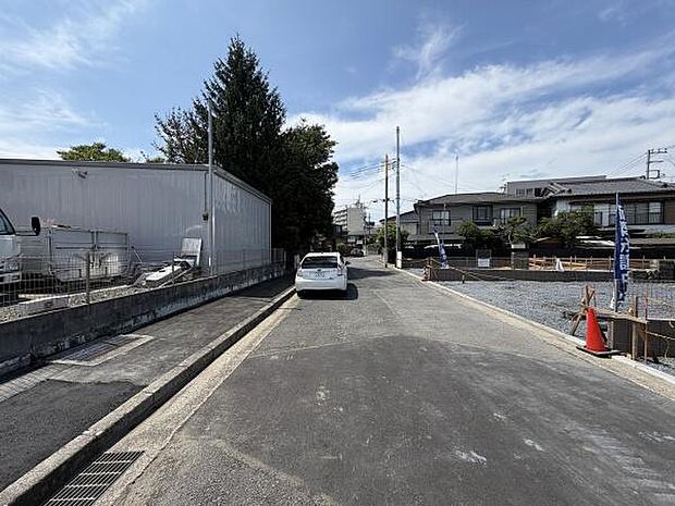 幅のある前面道路に面した現地の様子です。車の通行がしやすく敷地へのアプローチもスムーズです。周辺には住宅が建ち並び落ち着いた環境です。道路沿いに整備された歩道も確認できます。