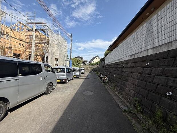 現地写真は青空と広がる前面道路が印象的です。道路幅がしっかり確保されており車両の出入りもスムーズに行えます。周囲は閑静な雰囲気で落ち着いた街並みが広がっています。