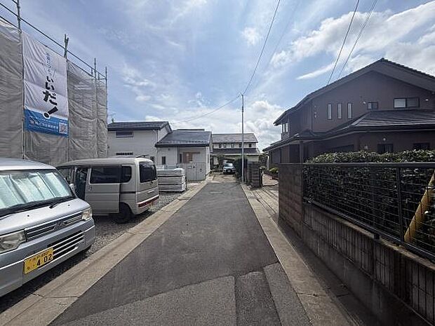 前面道路は舗装されており車両の通行もスムーズです。周囲には戸建て住宅が並んでいて落ち着いた雰囲気が感じられます。道路沿いには駐車スペースも整備されています。空を広く感じられる開放感があります。