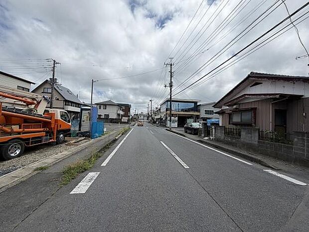 前面道路は広めで車の出入りもスムーズに行えます。周辺には住宅が立ち並び落ち着いた印象です。歩道も整備されていて歩行にも適しています。電柱や配線も整然としています。現地の様子が分かる写真です。