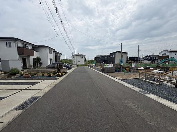 前面道路は幅があり車の出入りがしやすい印象です。周囲には新しい建物が並び整った街並みが広がっています。住宅地として落ち着いた雰囲気が感じられます。道路沿いの植栽もアクセントになっています。