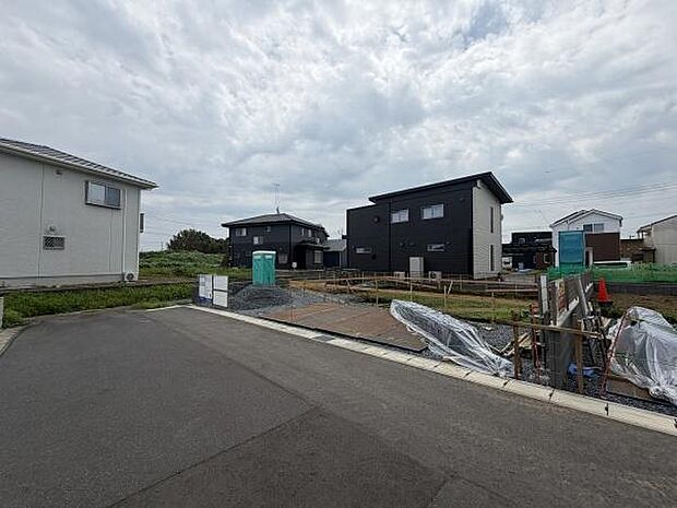 分譲地内の建築現場の様子です。周囲には新しい住宅が並び整然とした街並みが印象的です。道路幅も十分に確保されアクセスしやすい環境です。造成地ならではの開放感があります。