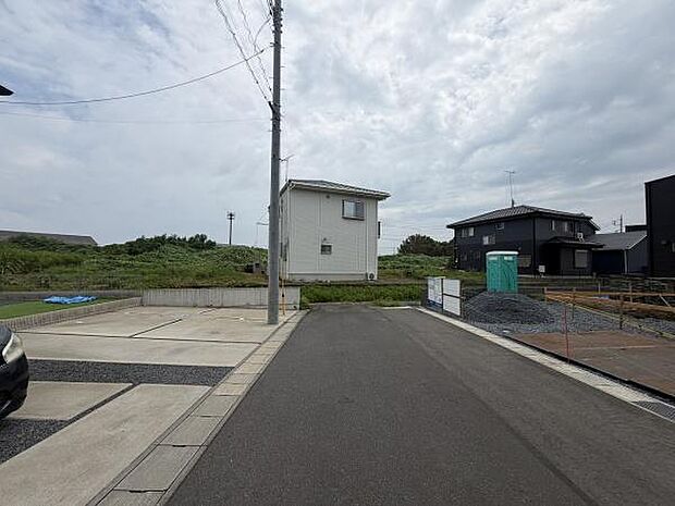 周辺は緑が広がり落ち着いた雰囲気の現地写真です。前面道路が整備されており車の出入りもスムーズです。両側に住宅や駐車スペースが並び道路幅も確保されています。現地の状況が一目でわかります。