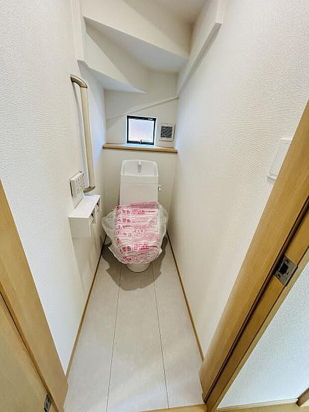コンパクトな空間に設置されたトイレです。上部に窓があり換気や採光が可能です。清潔感のある内装で使いやすい配置となっています。シンプルなデザインが特徴的です。