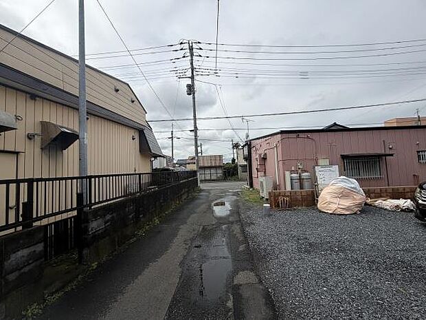 前面道路は舗装されており周辺には住宅や施設が立ち並んでいます。道幅があるため車両の出入りにも対応可能です。現地は落ち着いた雰囲気で電柱やインフラが整備されています。